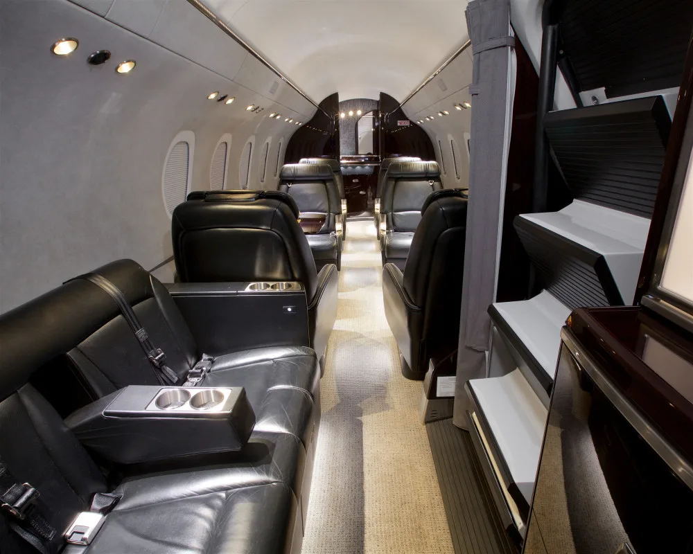 The luxurious interior cabin of a private jet features black leather seats and dark wood accents.