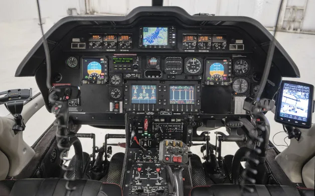 A detailed view of a helicopter's cockpit, featuring multiple digital displays, analog gauges, and flight controls.