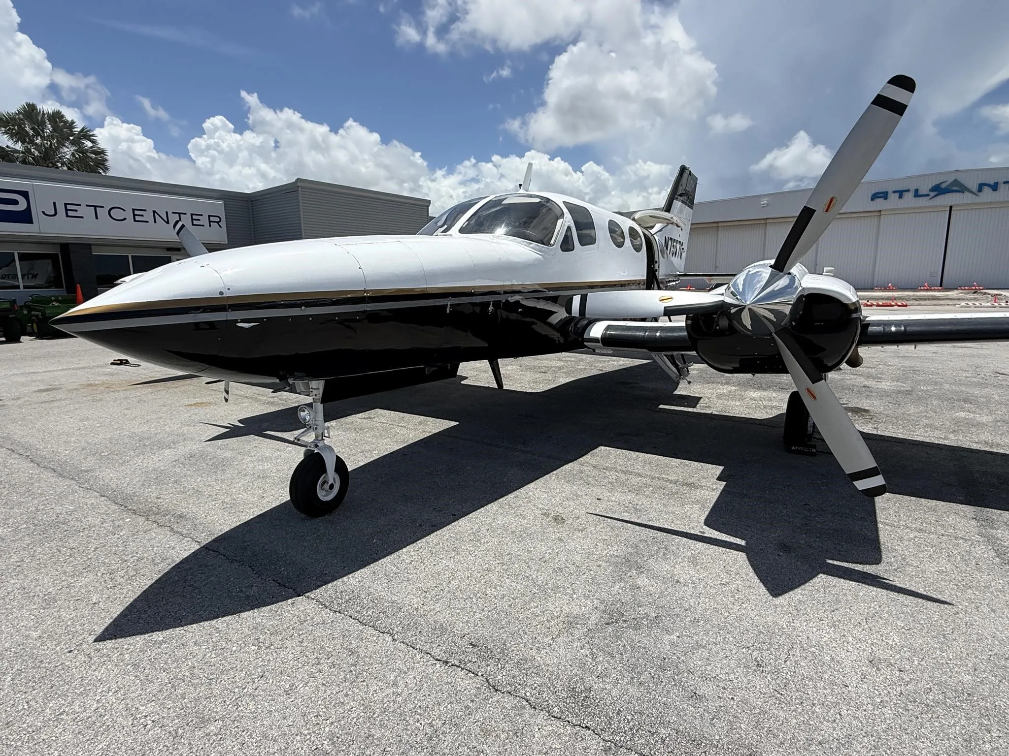 A front-side view of the white and black twin-engine propeller aircraft N7557Q on an airfield.