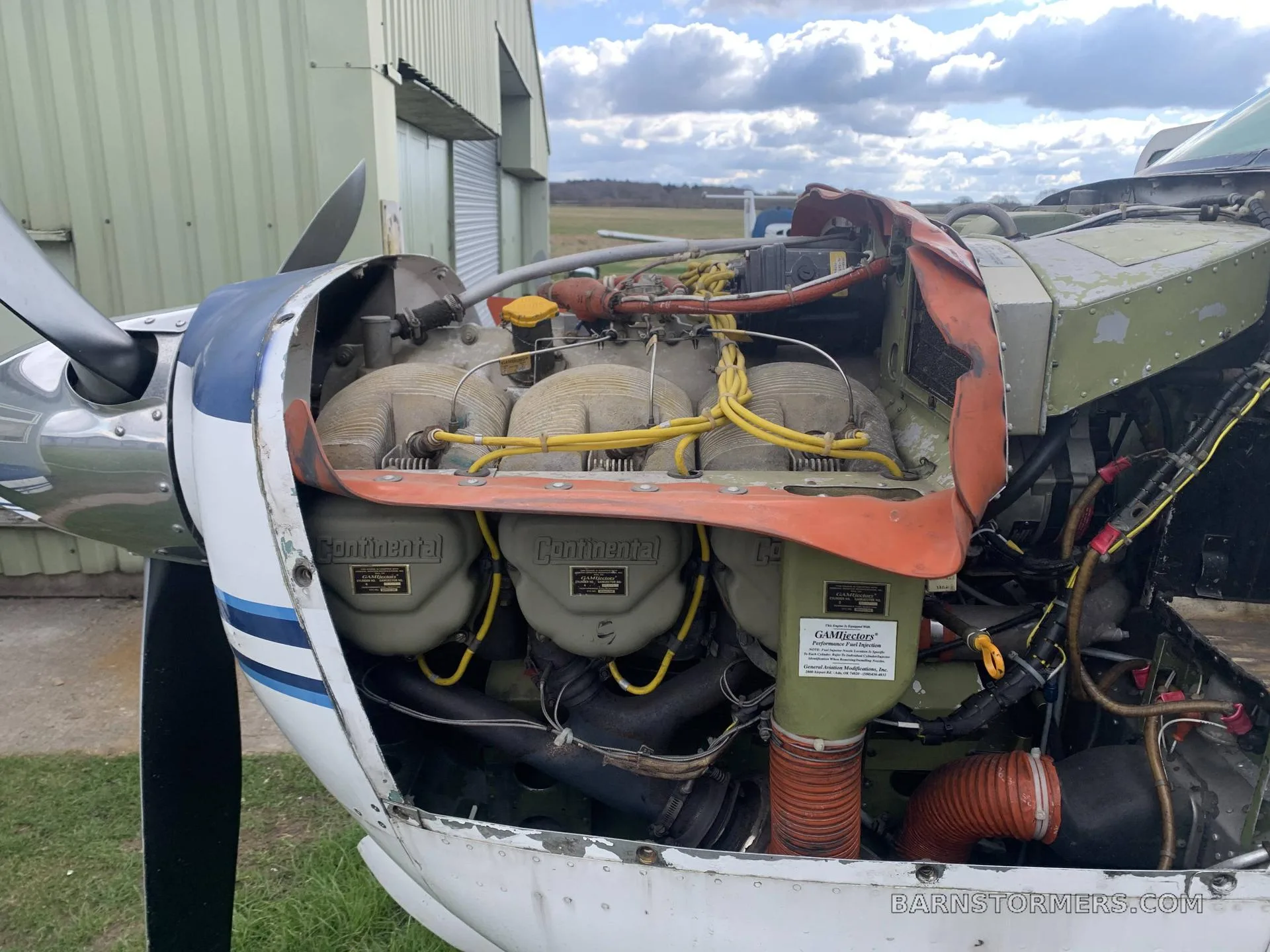 A close-up view of a Continental aircraft engine with yellow ignition wires and exposed cylinders, with the cowling removed.