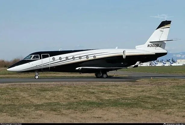 A Gulfstream G200 business jet with registration N300BJ, featuring a black and white paint scheme with gold accents, parked on an airfield.