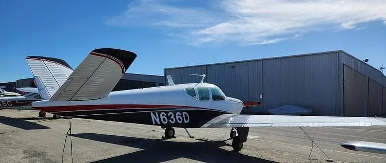 A white and black single-engine aircraft with red stripes, tail number N636D, parked on an airport tarmac next to hangars.