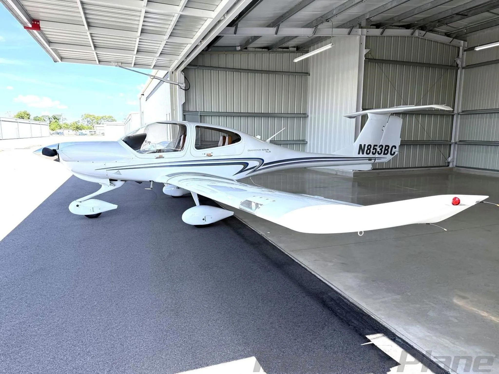 A white Diamond Star DA40 XLS aircraft with blue and grey stripes, tail number N853BC, parked partially in a hangar.