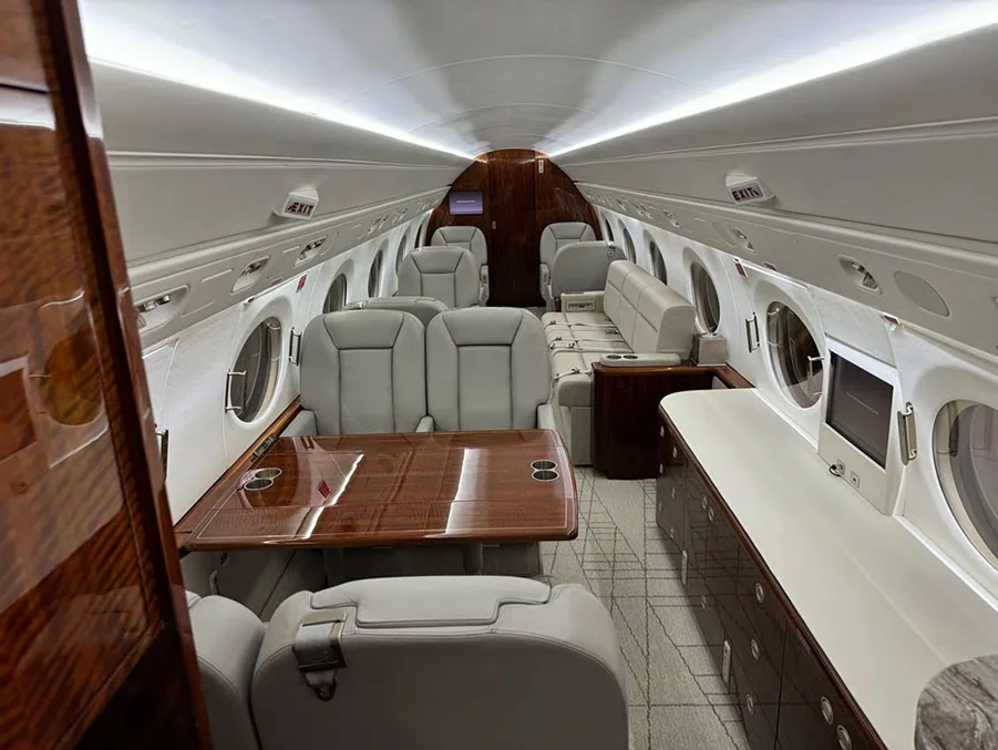 A luxurious aircraft cabin with light gray leather seats, a wooden table, and dark wood cabinetry.