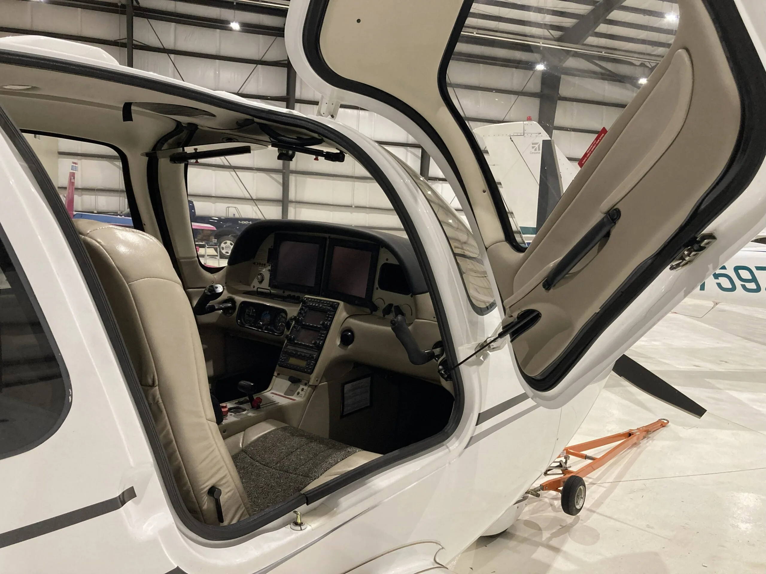 View into the open cabin of a Cirrus SR22 aircraft, showing beige seats and the cockpit.