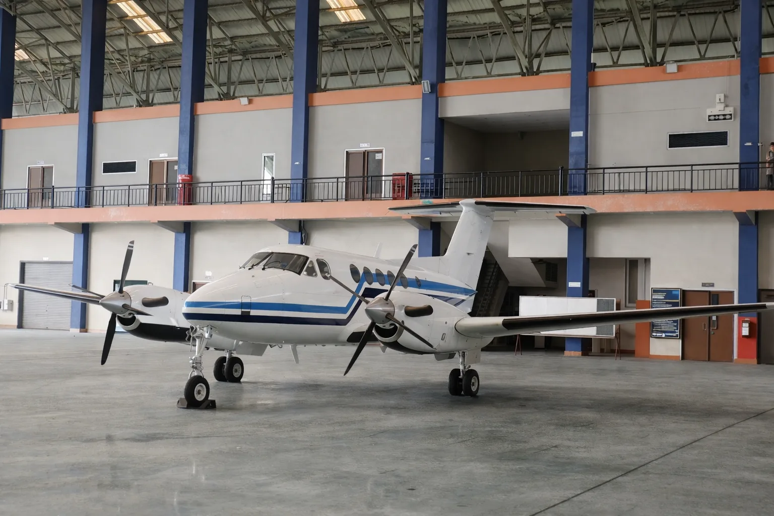 A white and blue twin-turboprop aircraft, likely a Beechcraft King Air, parked inside a large hangar.
