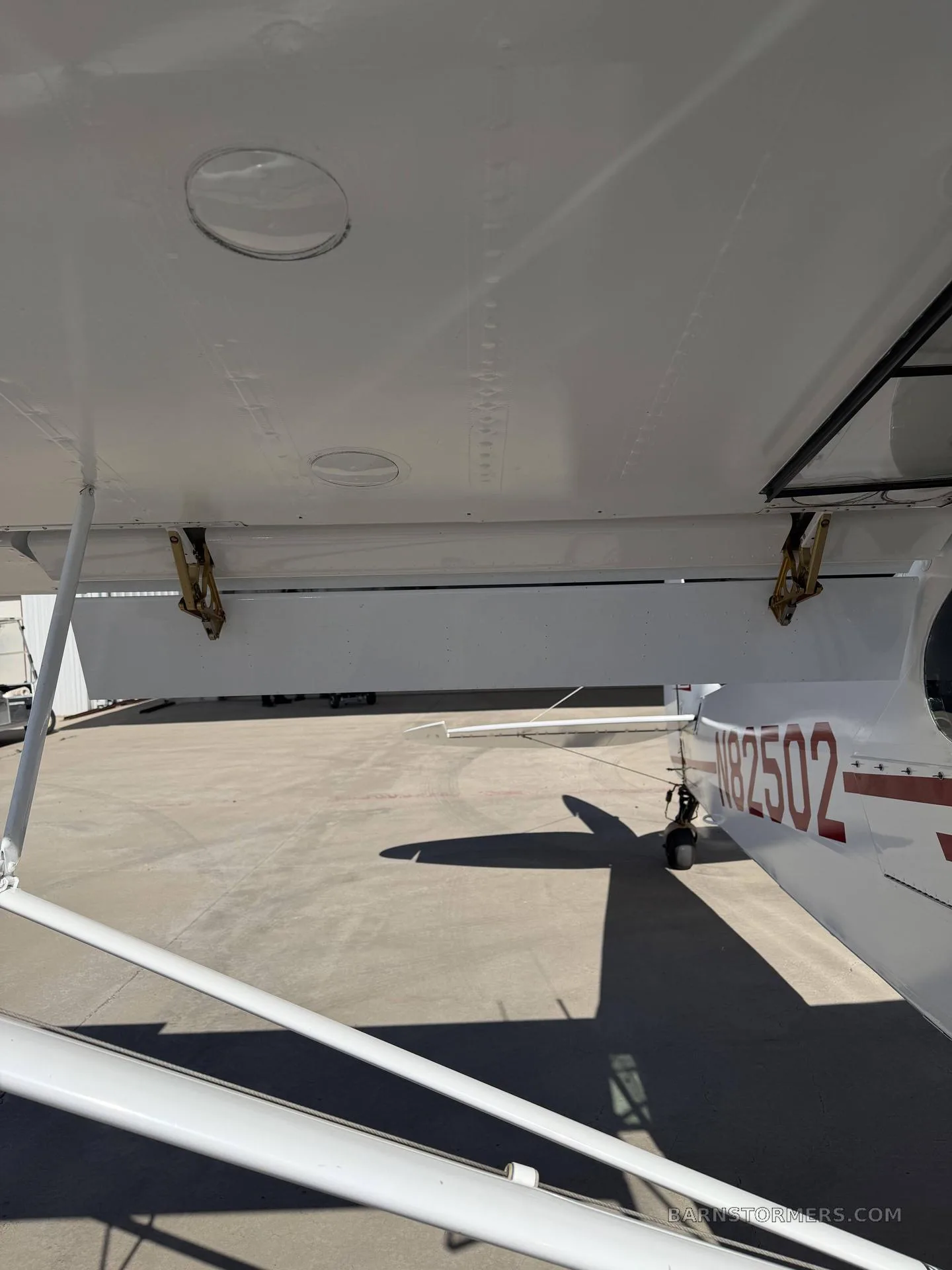 An underside view of the white wing of a bush plane, showing the flap and the N-number on the fuselage.