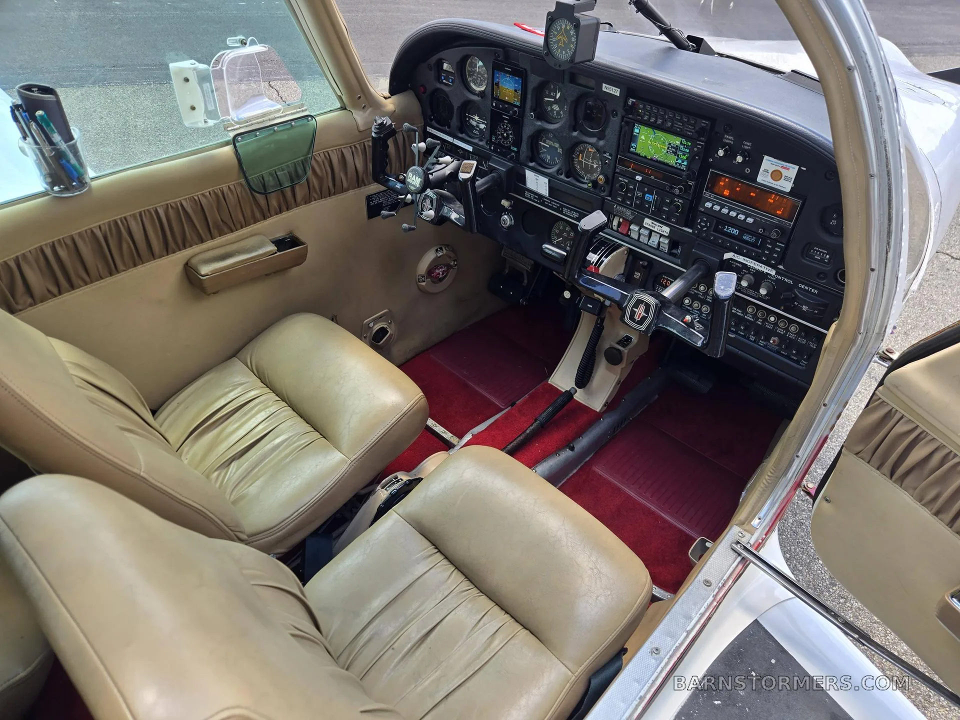 The tan leather seats and red carpeted floor of a small aircraft cabin are visible, with the instrument panel and controls in the foreground.