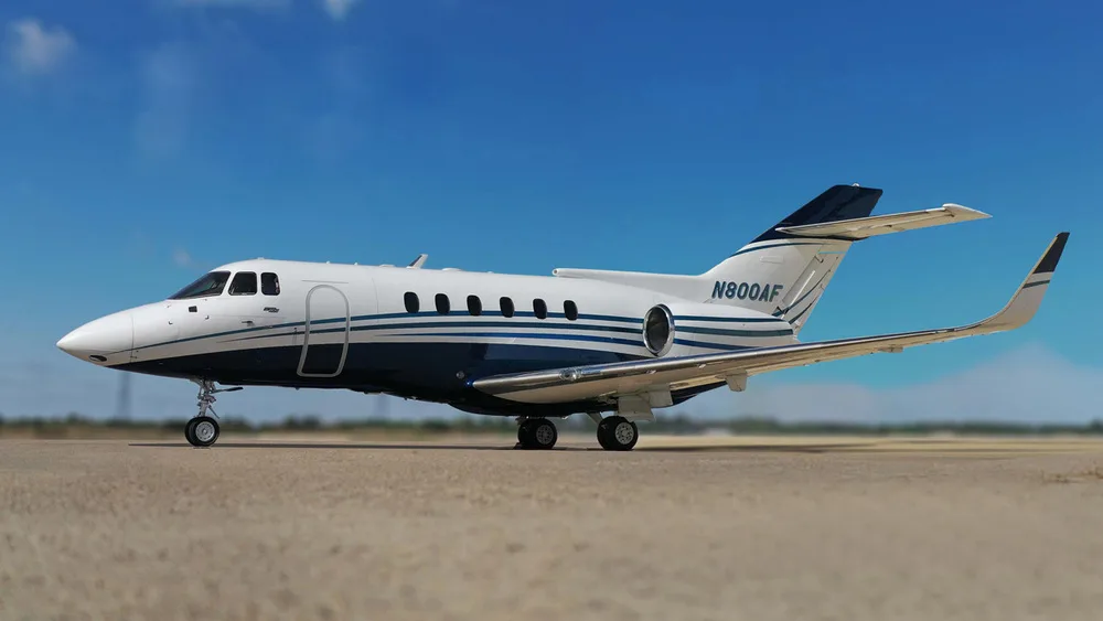 A white and blue Hawker 800XP business jet, registration N800AF, parked on an airfield under a blue sky.