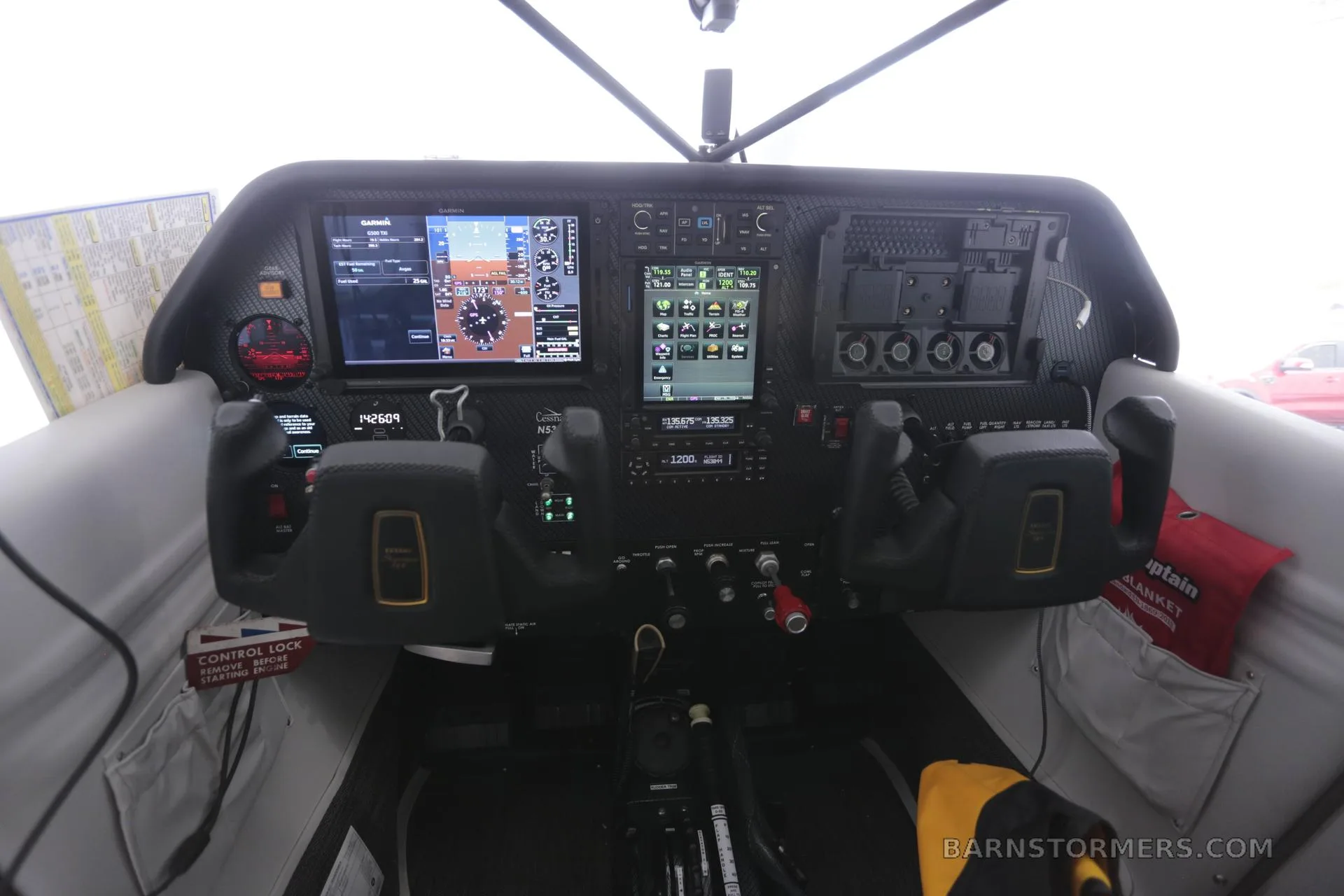 The cockpit of a Cessna 180 Skywagon, featuring a modern glass panel with Garmin displays and dual yokes.