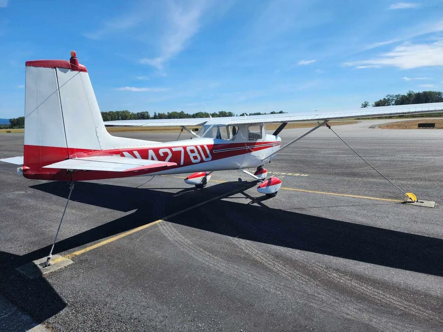 A white and red Cessna 150 aircraft with registration N4278U parked on an asphalt ramp under a clear blue sky, viewed from the rear-left.