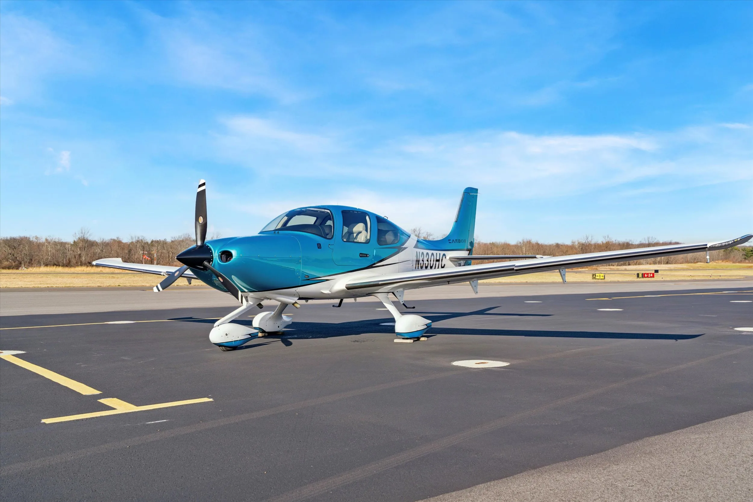 A front-quarter view of a teal and white Cirrus SR22 aircraft, registration N330HC, parked on an airfield.