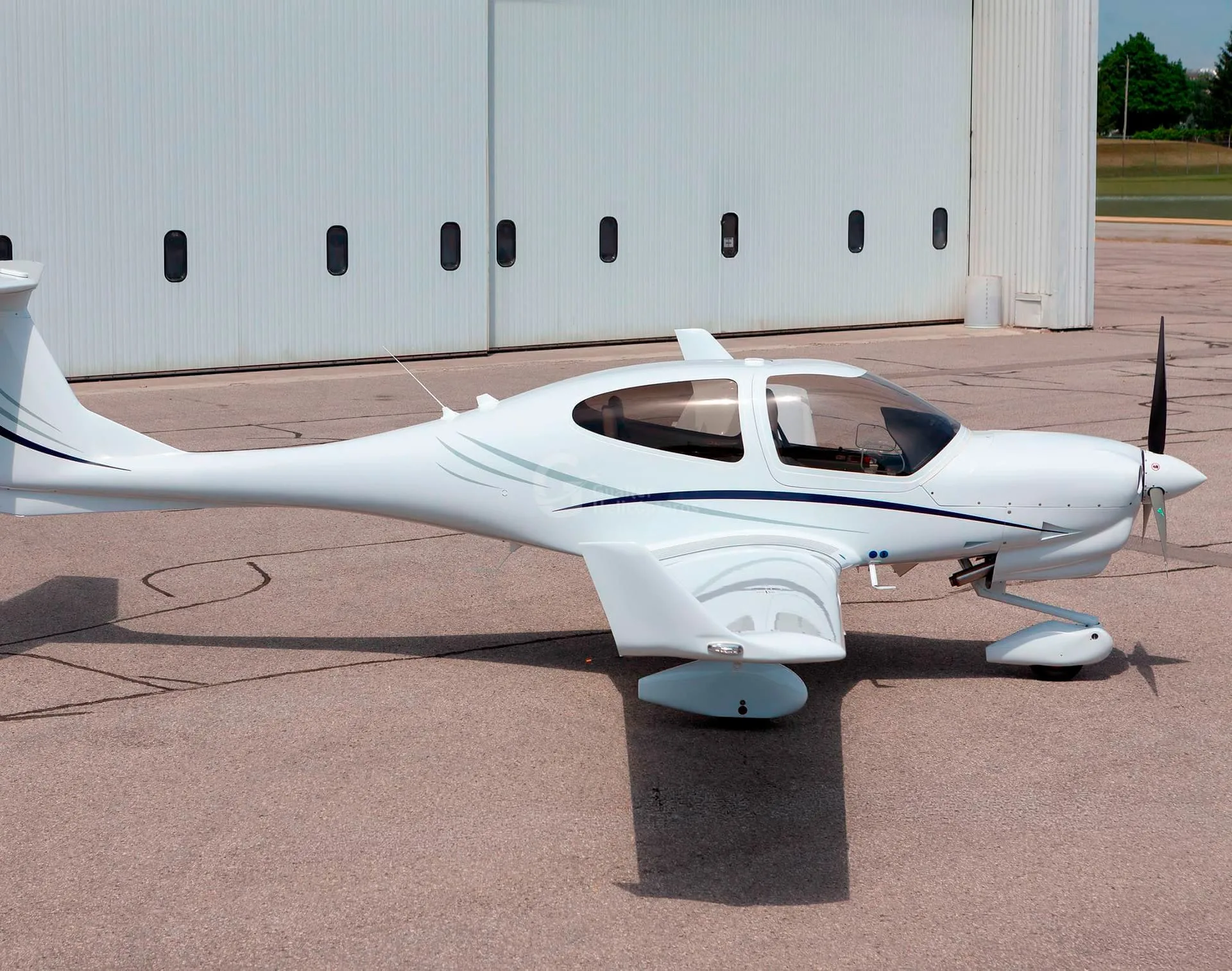 A white Diamond DA40 aircraft with blue and grey stripes parked on an asphalt apron, viewed from the side.