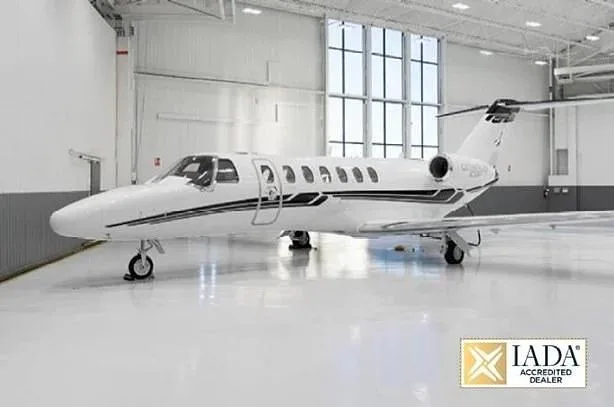 A white Cessna Citation M2 business jet with black stripes is parked inside a bright hangar.