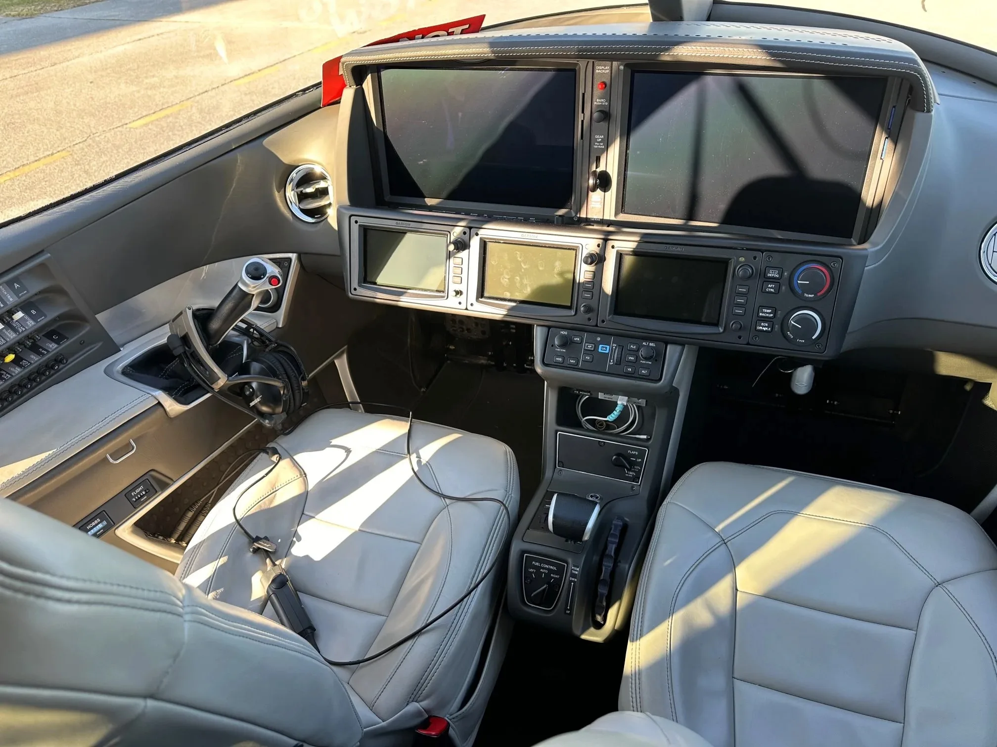 The cockpit of a Cirrus Vision Jet, showing the instrument panel with multiple screens and light gray leather seats.