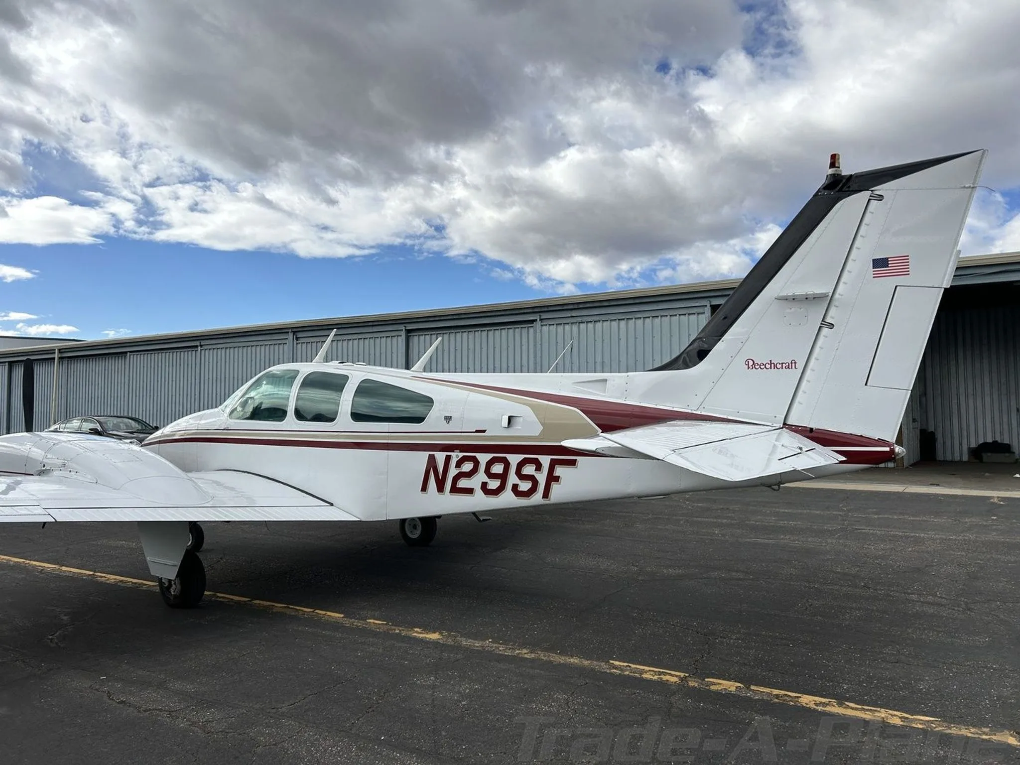 A rear-side view of the white and maroon Beechcraft Baron N29SF, showing the tail and rear fuselage, parked on an asphalt ramp.