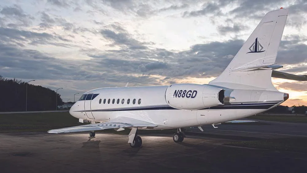 A rear-quarter view of the white business jet N88GD with a dark blue stripe, parked on an tarmac at sunset.