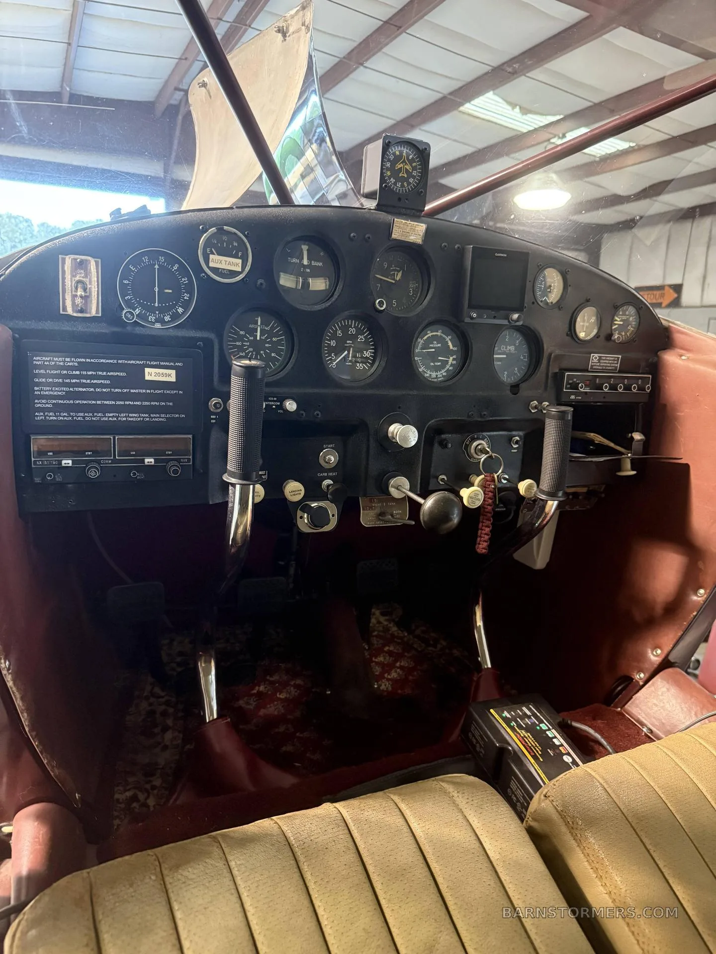 The cockpit of an aircraft, showing a black instrument panel with various gauges, a yoke, and tan seats with a patterned floor.