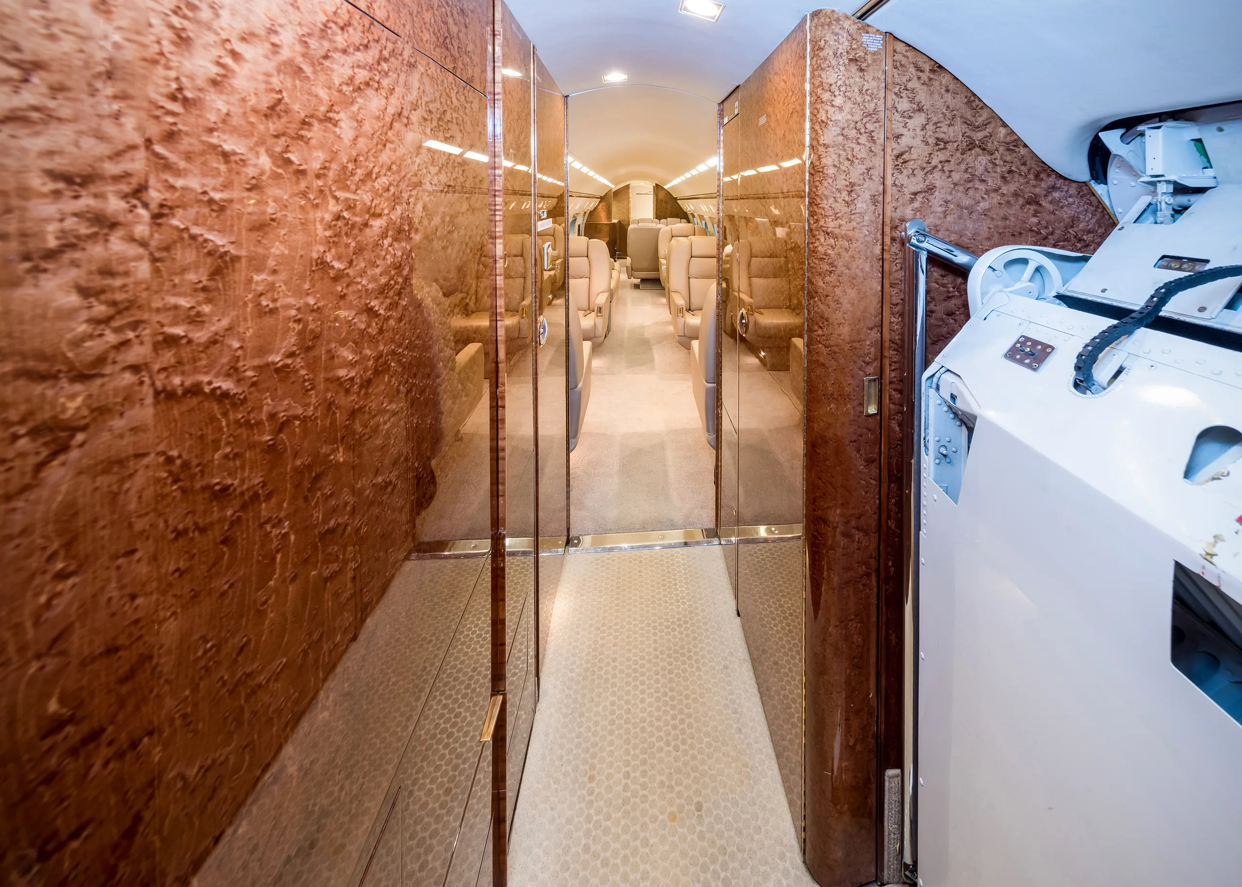 A view down the aircraft cabin aisle, showing wood-paneled walls and beige seats in the distance.