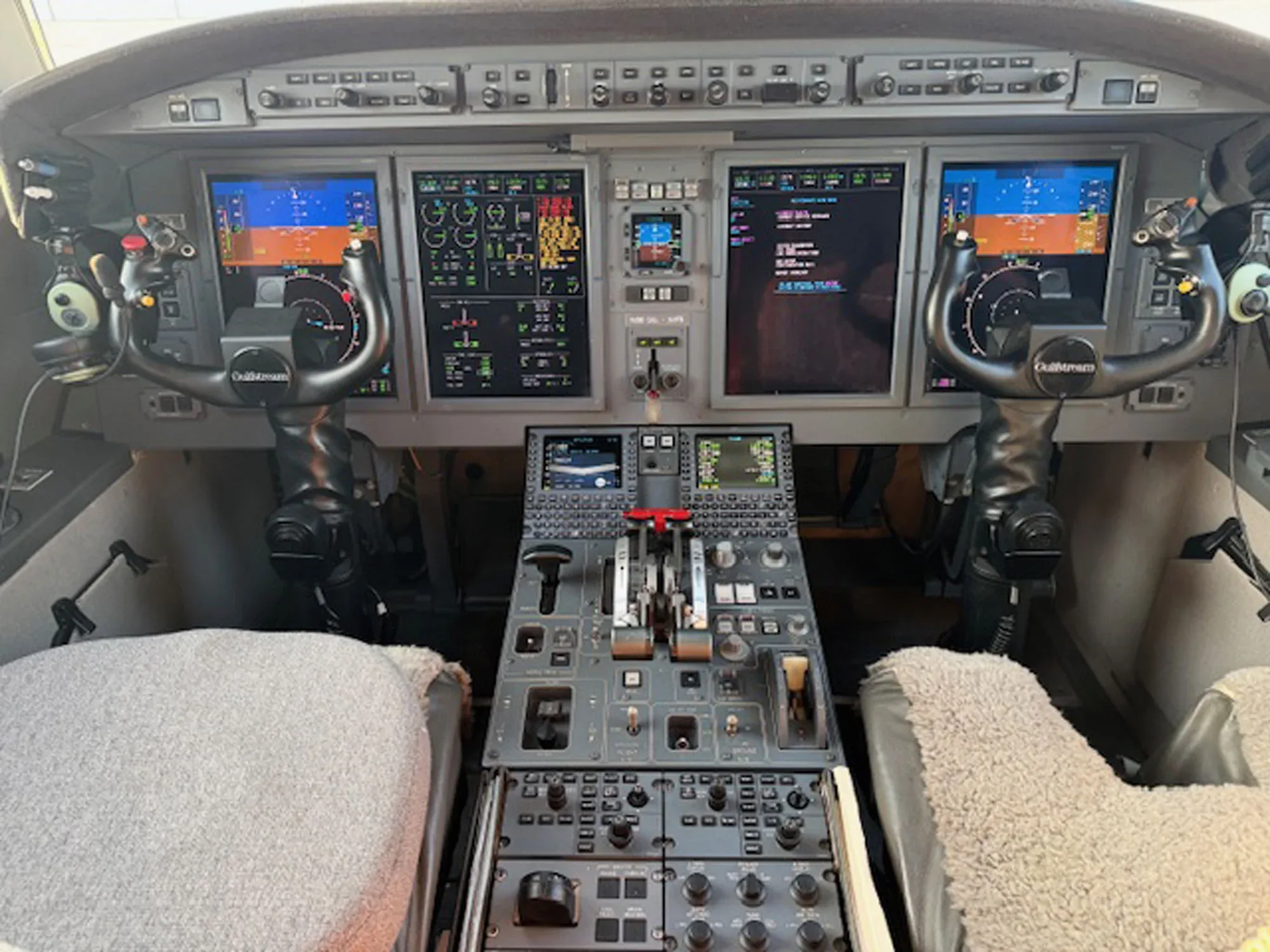 The modern glass cockpit of a private jet, featuring multiple display screens and control yokes.