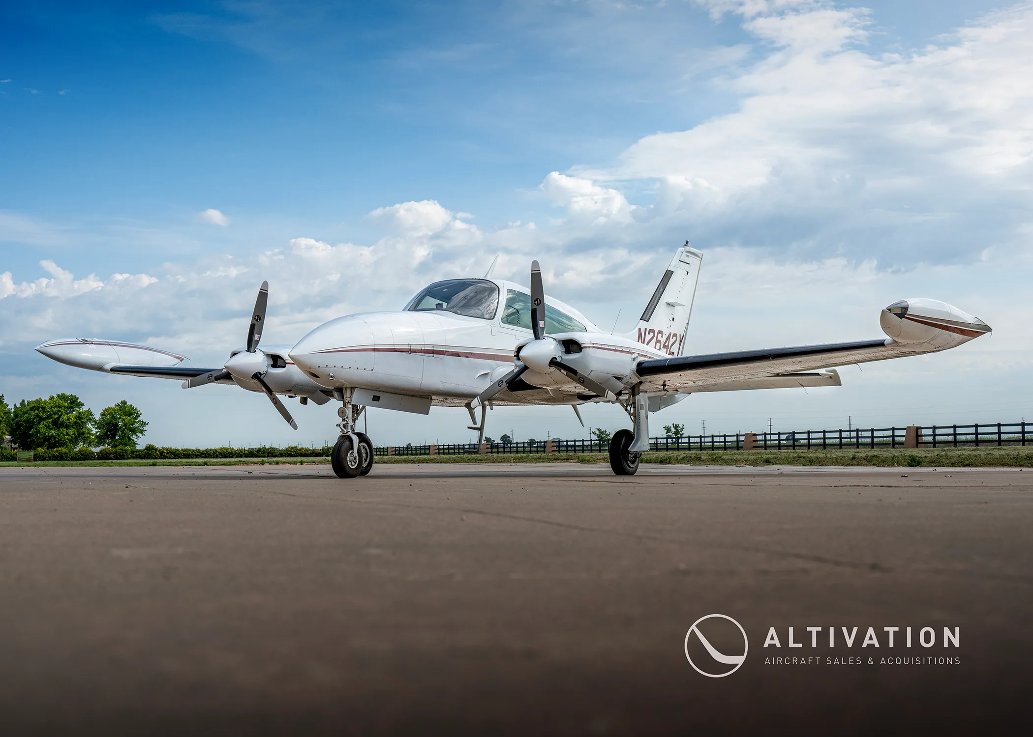 A low-angle view of a white twin-engine propeller aircraft with red and grey stripes, registration N2642Y, parked on an airfield.