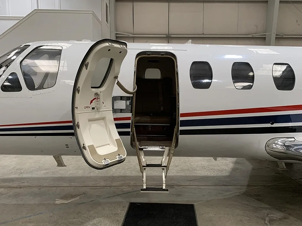 A close-up view of the open main entry door and integrated stairs of a white business jet.