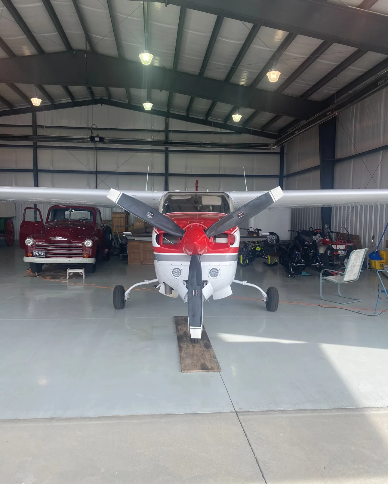 Front view of a red and white propeller aircraft inside a hangar with a vintage truck.