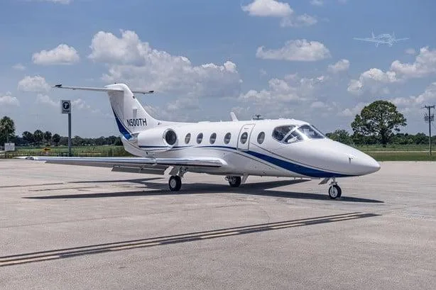 A white business jet with blue stripes, registration N500TH, parked on an airport tarmac with trees in the background.