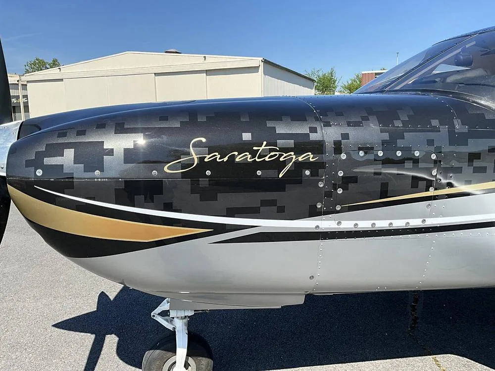 Close-up of the nose of a Piper Saratoga, showing the black, silver, and gold paint scheme with "Saratoga" written on the side.