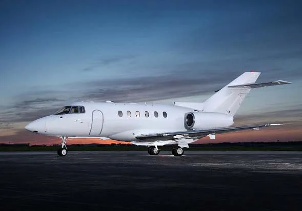 A white business jet, possibly a Hawker, sits on a tarmac at sunset.