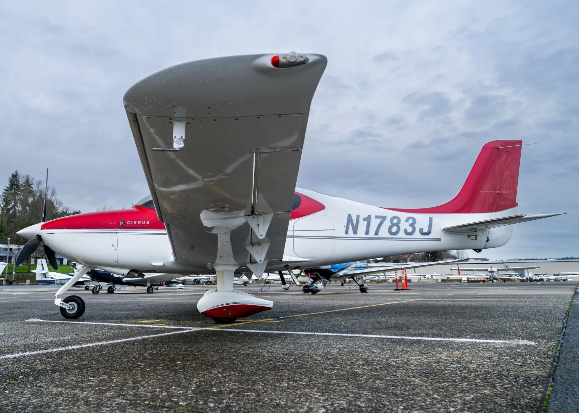 A rear-side view of the red and white Cirrus SR22 aircraft, N1783J, with its wing up, parked on a tarmac.
