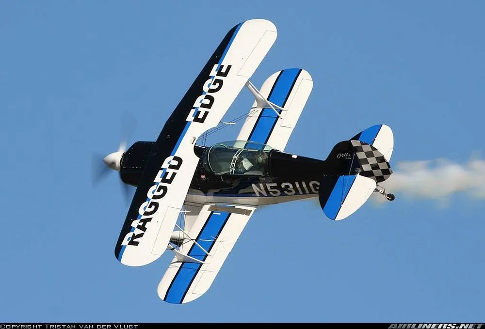A black, white, and blue Pitts biplane with registration N5311G is flying inverted against a blue sky.