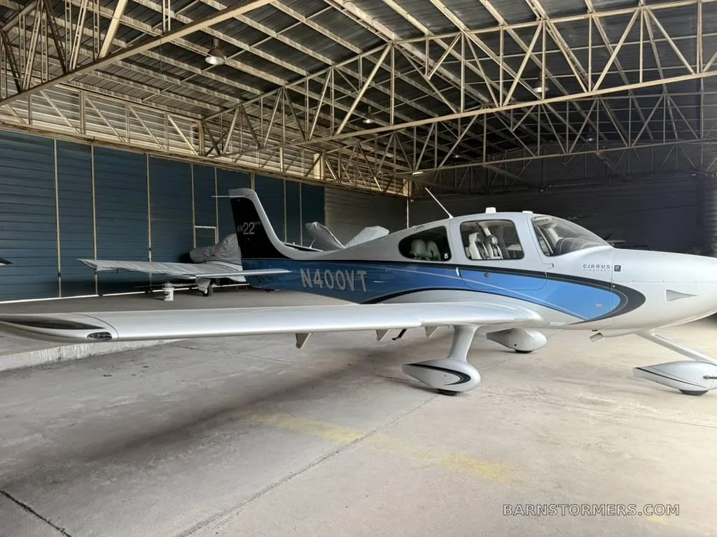 A side view of a white and blue Cirrus SR22 aircraft, registration N400VT, parked inside a hangar.