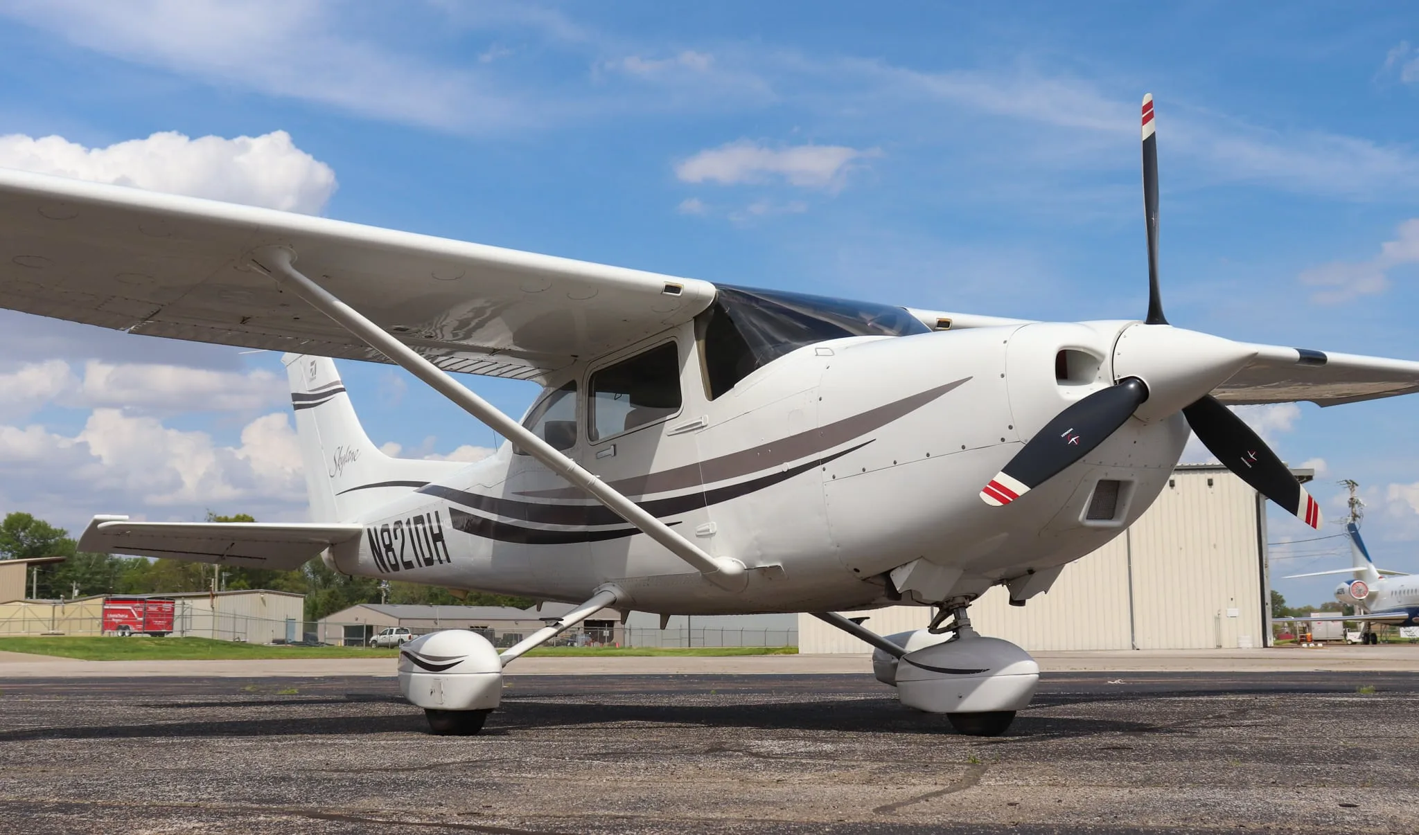 A close-up front-right view of the white Cessna Skylane N821DH with its propeller, parked on an asphalt tarmac.