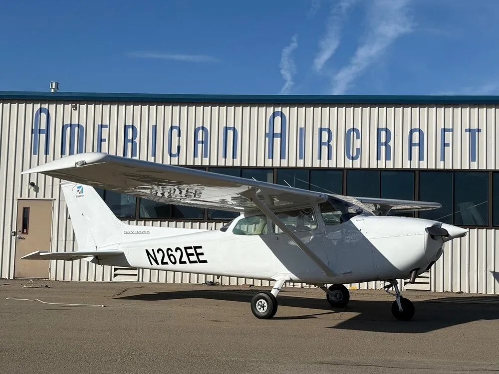 A white Cessna Skyhawk N262EE parked on an tarmac in front of a hangar.