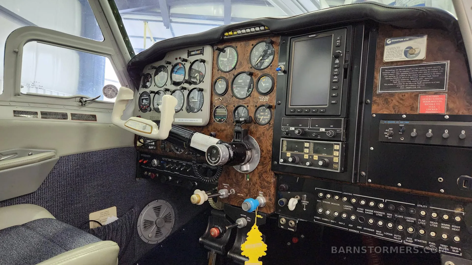 A close-up view of an aircraft cockpit with a wood-grain instrument panel, multiple gauges, and a Garmin display.