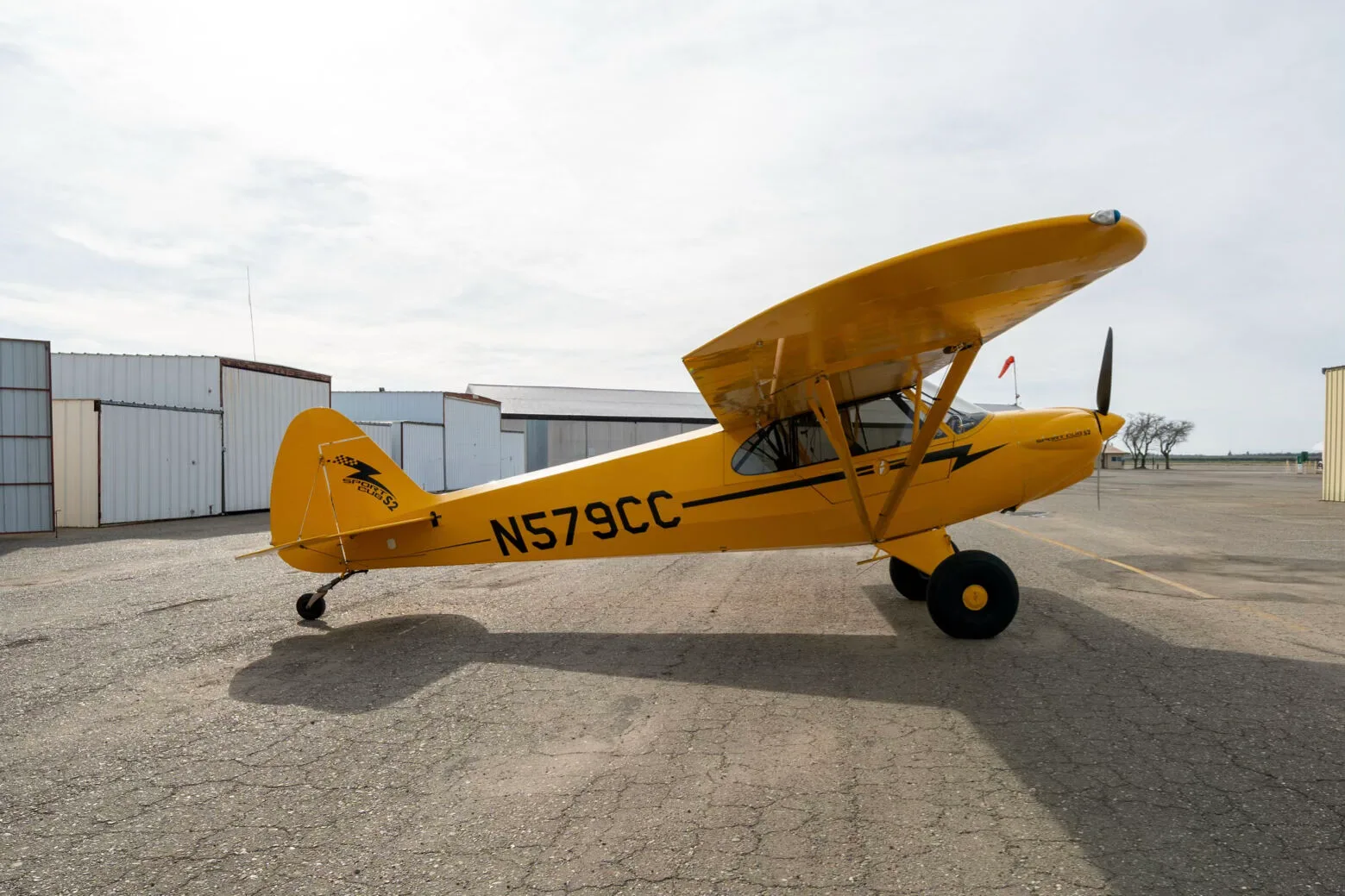 A yellow CubCrafters Sport Cub S2 aircraft with registration N579CC parked on an airfield, viewed from the rear-right.