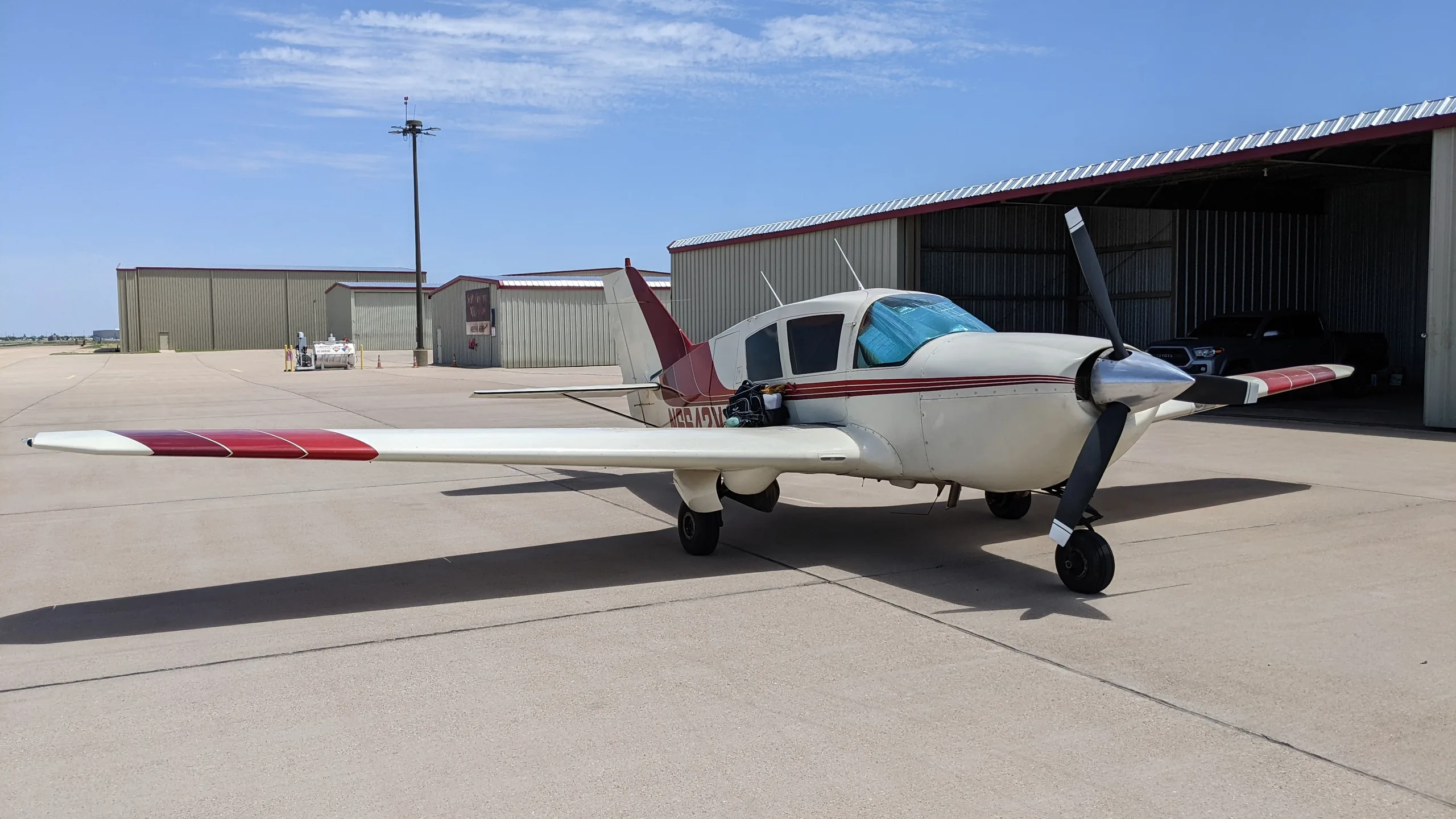 A white and red Bellanca aircraft parked on an airfield tarmac next to a hangar under a clear sky.