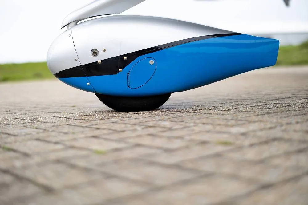A close-up of the blue and silver wheel fairing and landing gear of a Cirrus SR22T GTS on a paved surface.