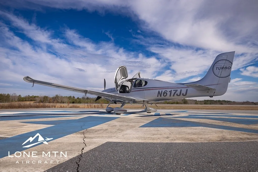 A silver Cirrus SR22T aircraft, N617JJ, with its doors open, parked on an airfield from a low angle.