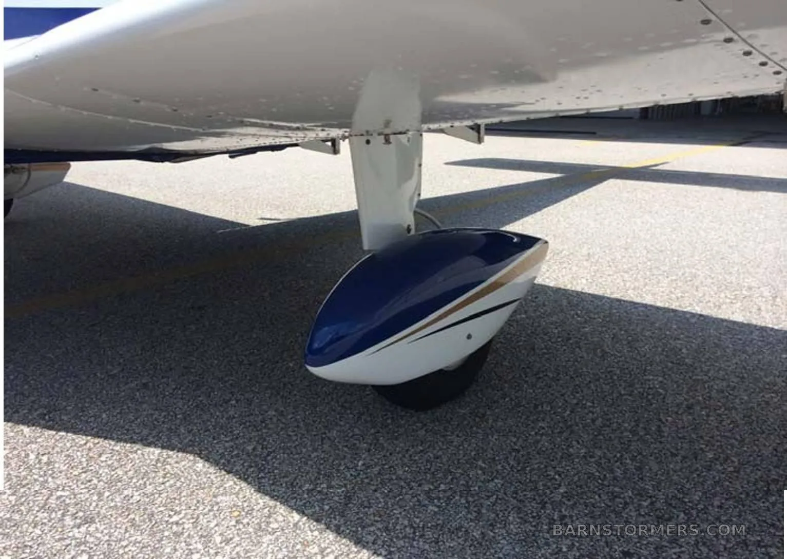 A close-up view of the main landing gear and wing of a white and blue aircraft.