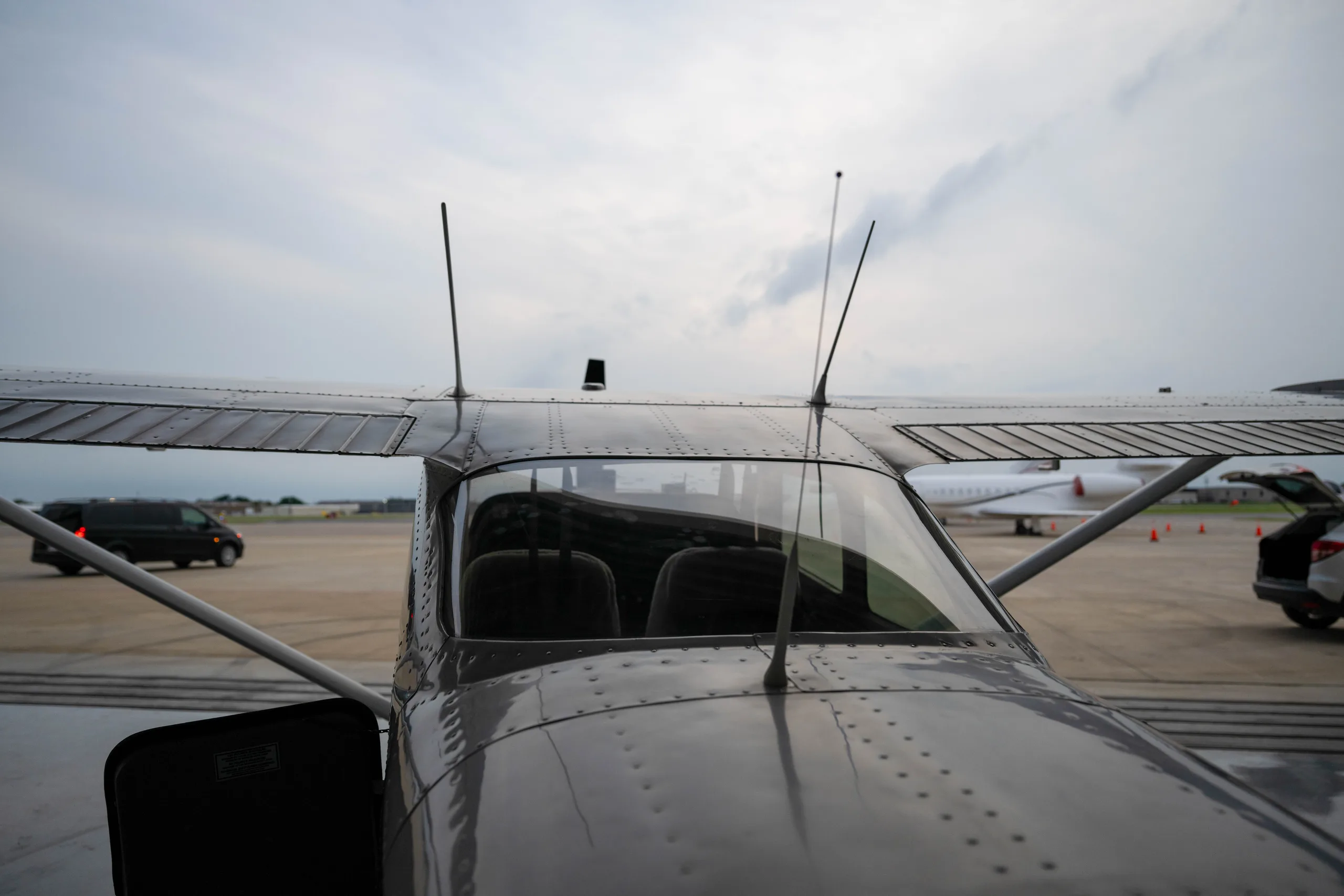 A front view of a white aircraft with its door open, parked on an airport tarmac under a cloudy sky.