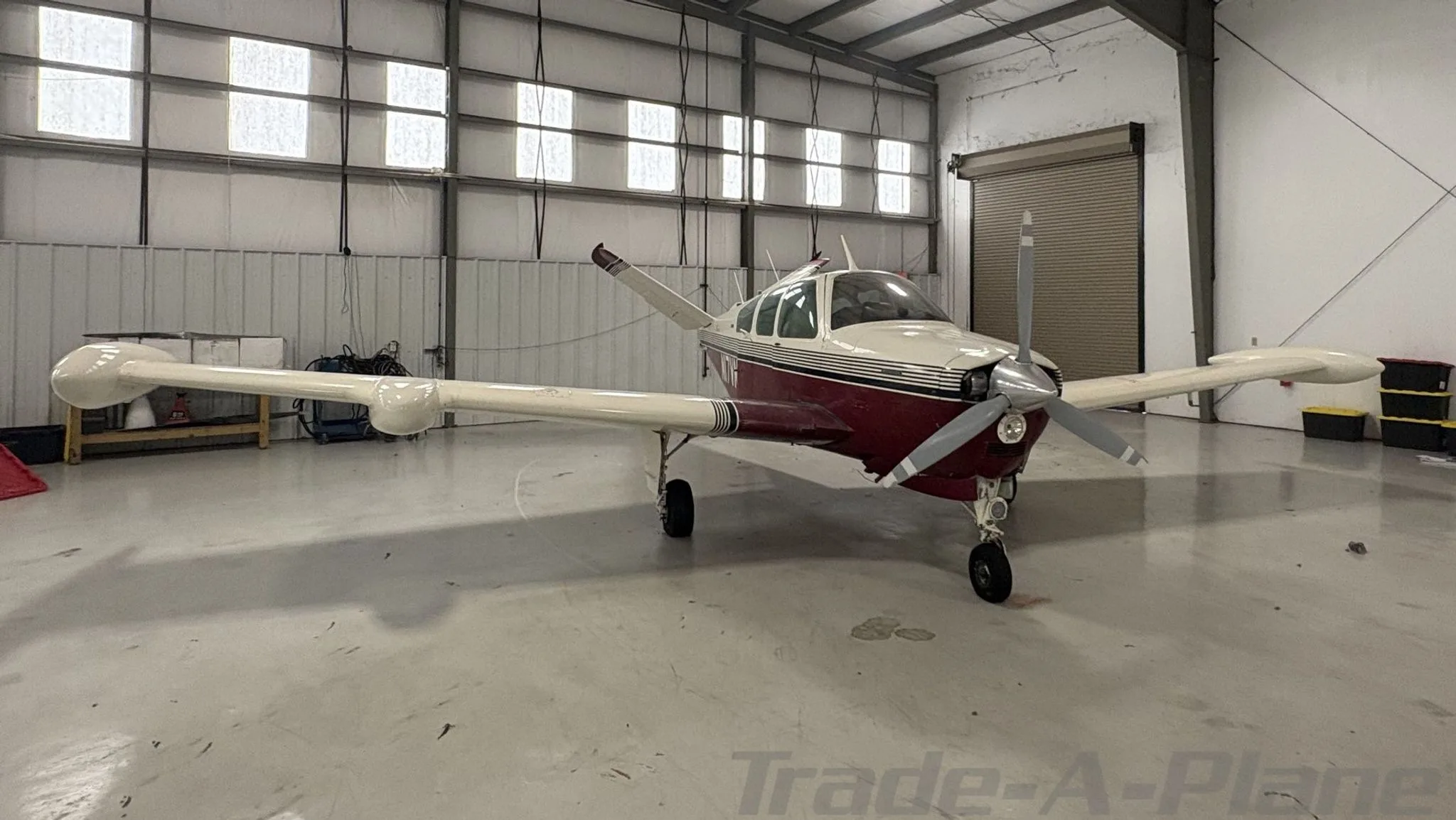A white and maroon Beechcraft Bonanza N17VM parked inside a hangar, viewed from the front-left.