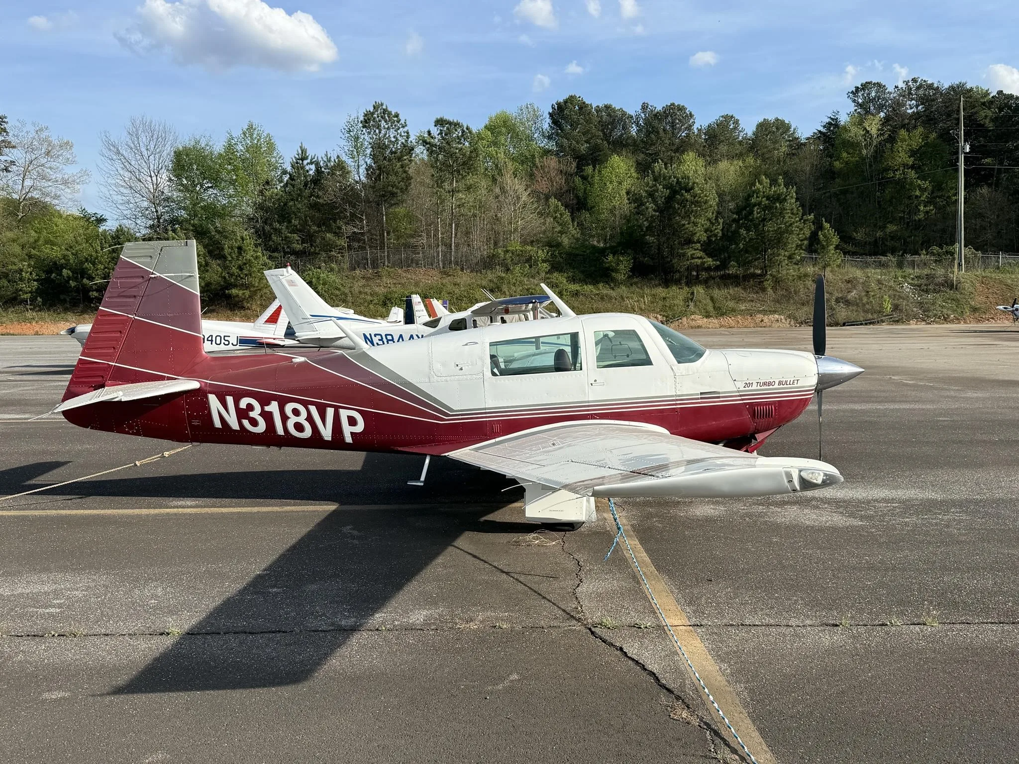 A red and white Mooney 201 Turbo Bullet aircraft, N318VP, parked on an asphalt ramp, casting a long shadow.