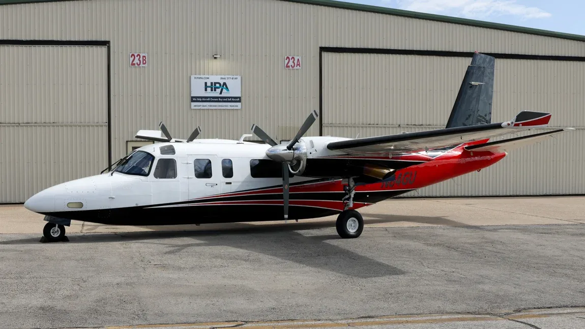 A white, black, and red twin-engine aircraft, N84GU, parked on an tarmac in front of a hangar.