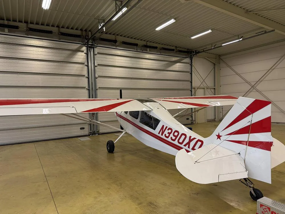 Rear view of a white single-engine aircraft with red stripes and a red star on the tail, parked inside a hangar.