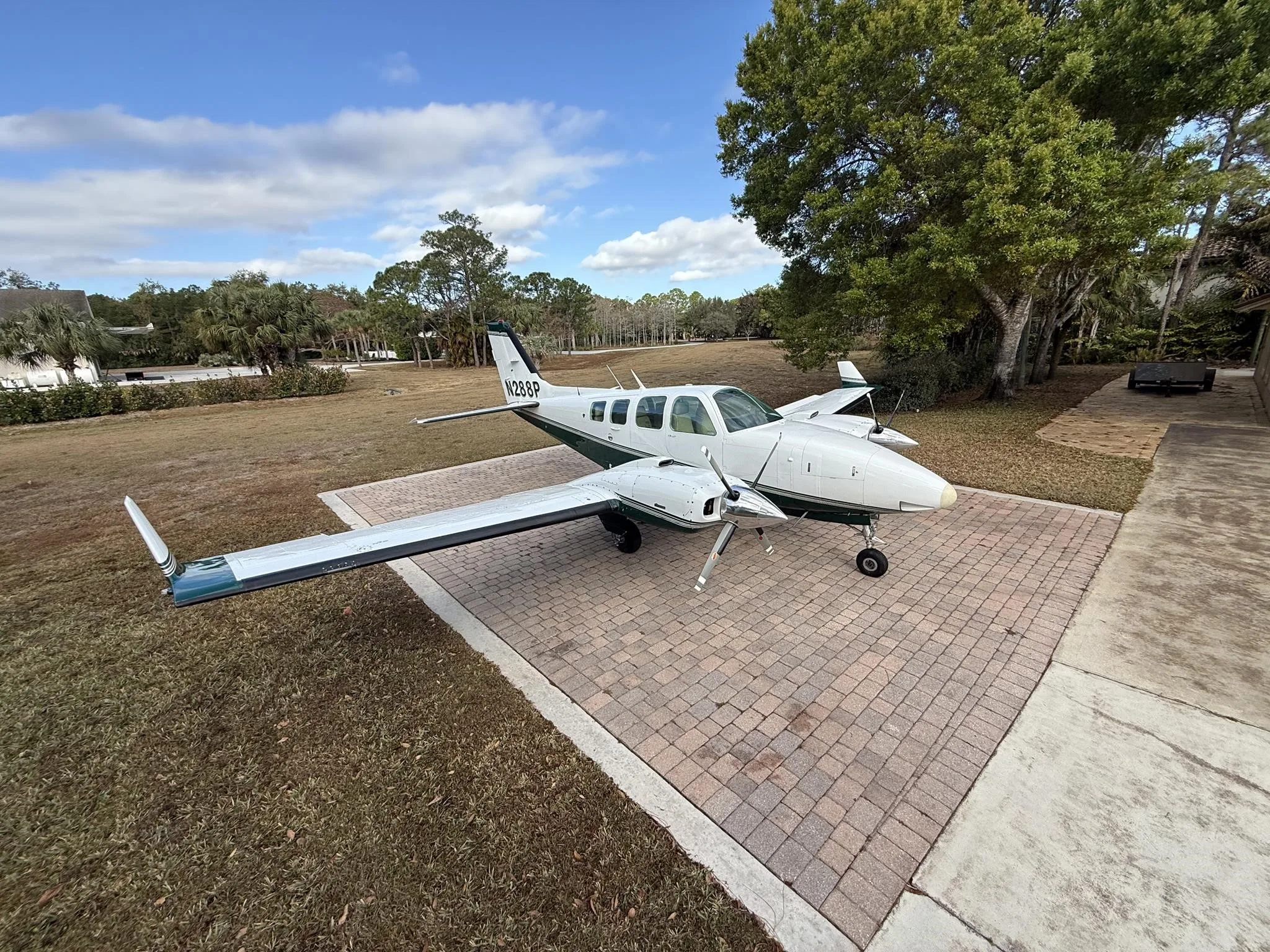 A white and green twin-engine Beechcraft Baron aircraft with tail number N288P parked on a brick driveway.