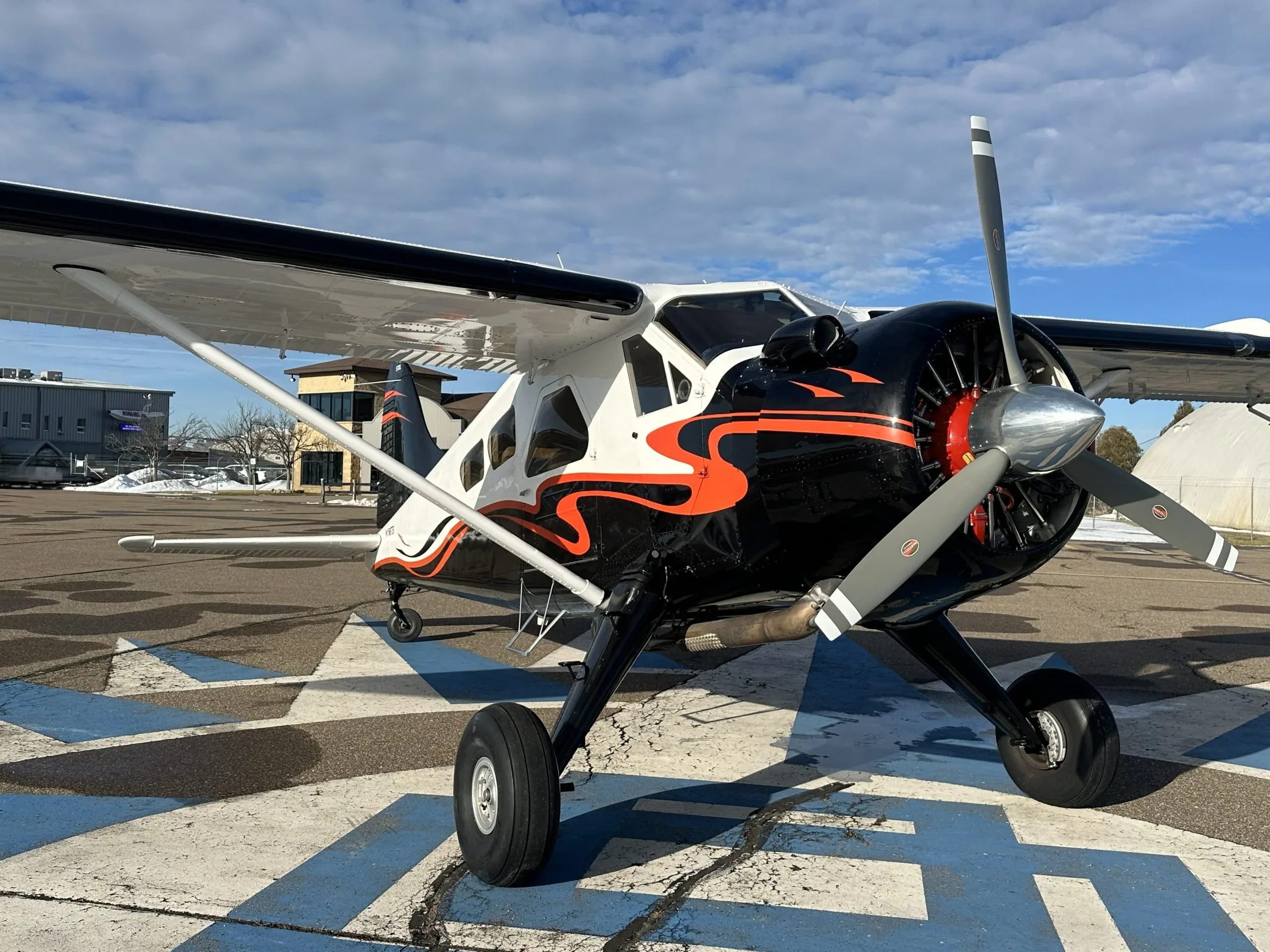 Front-right view of a white and black single-engine turboprop aircraft with orange accents on an airfield.