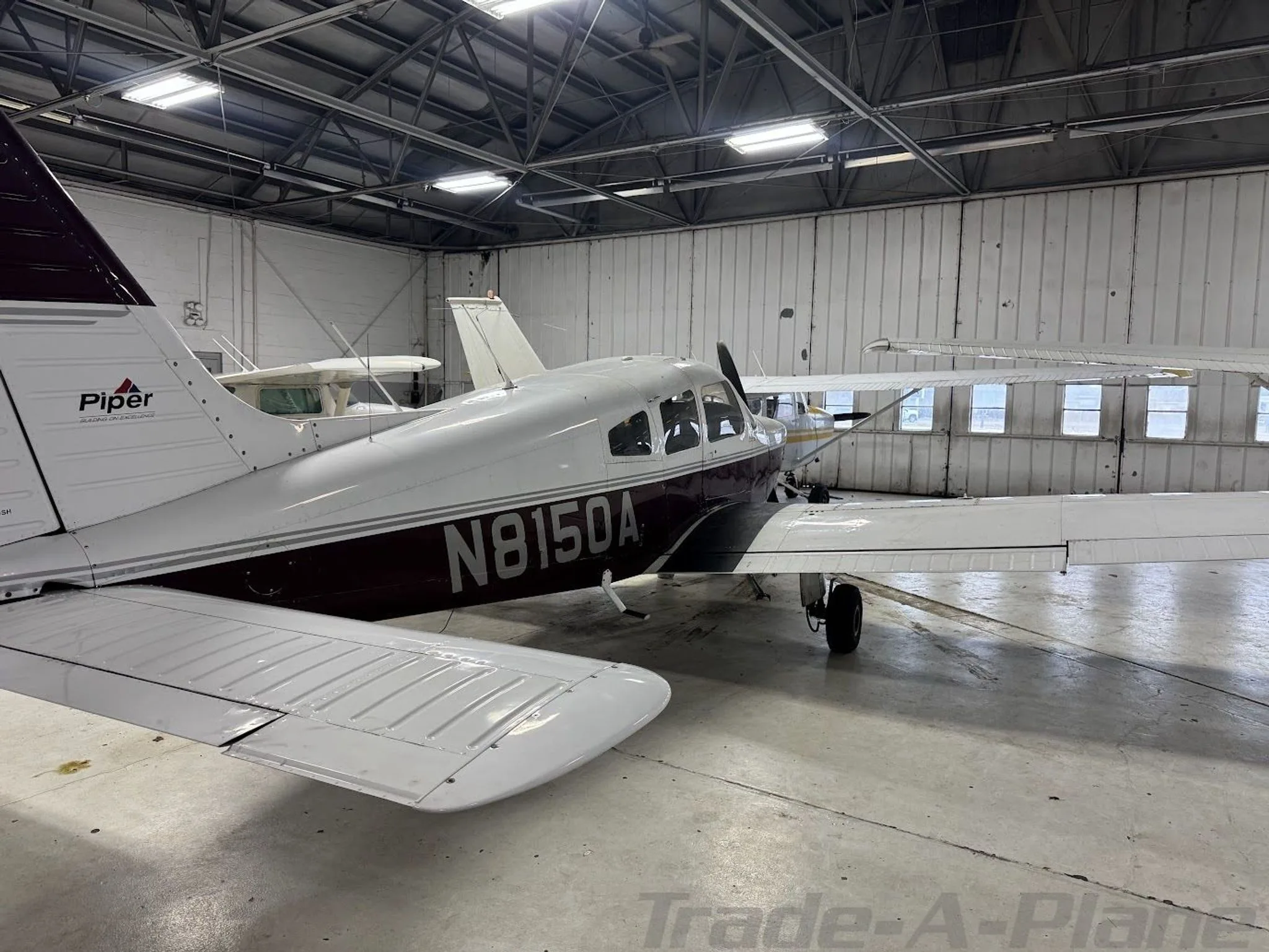 A white and maroon Piper Archer II (N8150A) parked in a hangar, viewed from the rear-left.