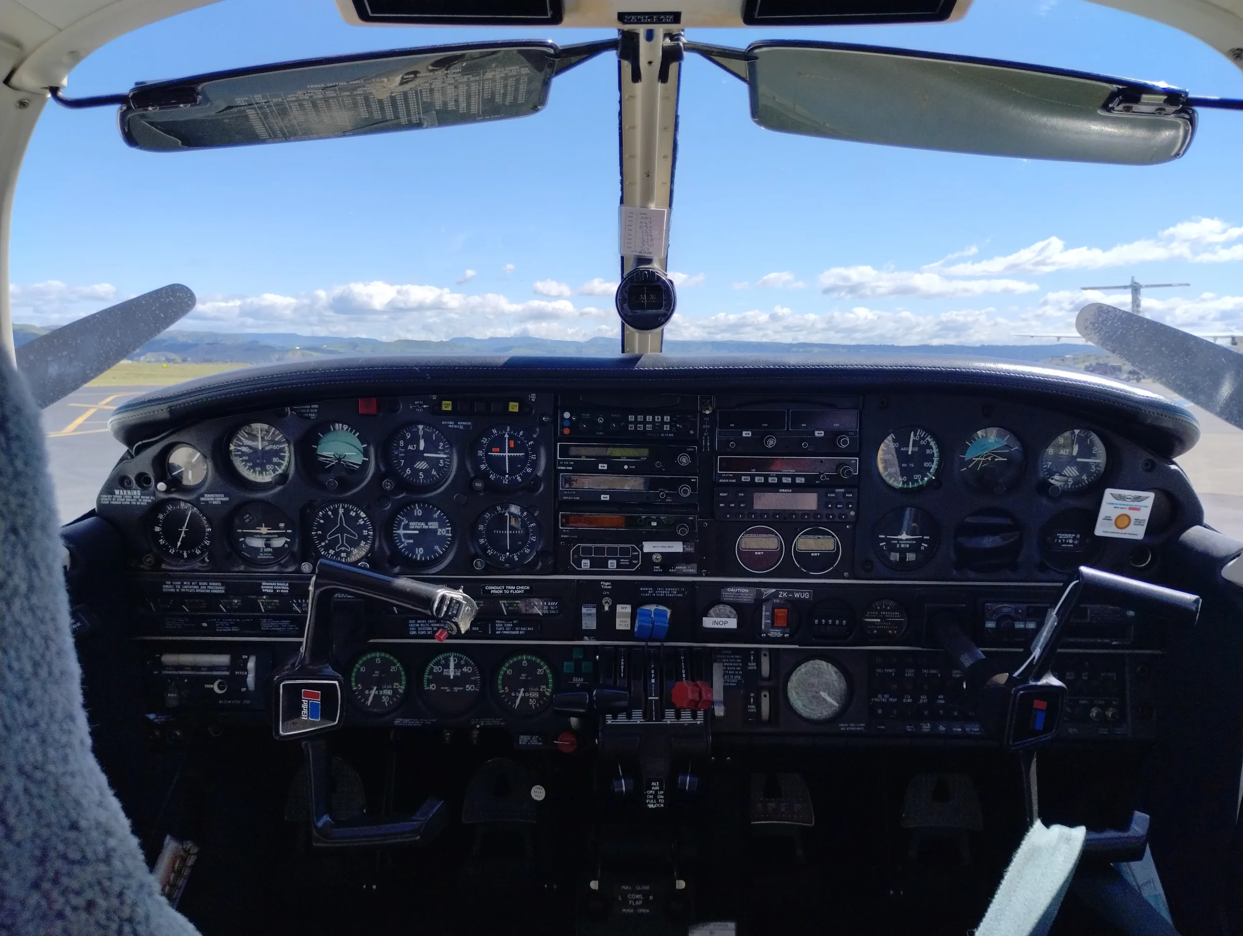 The cockpit of a small aircraft with numerous analog gauges and a view of the runway and sky through the windshield.